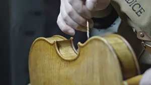 A hand is working on a violin, highlighting craftsmanship and wooden texture