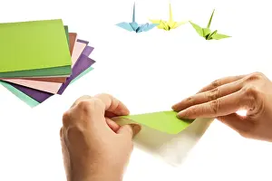 Hands folding green origami with colorful paper cranes in the background