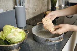 Hands gently hold a piece of duck above a cooking pot in a contemporary kitchen