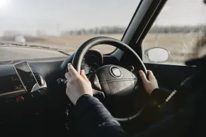 Hands on a steering wheel with sunlight illuminating the interior during a drive