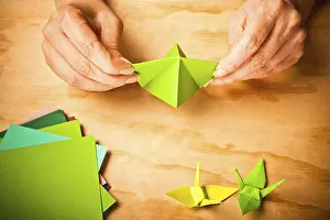 Hands working on green origami crane with colored paper nearby