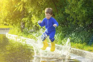 A happy boy in rubber boots jumps in puddles