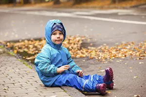 Happy child in waterproof coat and rainboots outdoors in autumn season