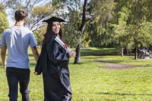 Happy graduated girl walking whitle holding hands with her boyfriend while she turns arround to show her diploma