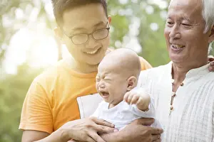 Happy grandfather, father and crying baby grandchild at outdoors park