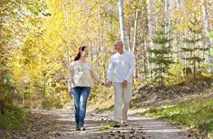 Happy married couple - husband and his pregnant wife walk in autumn forest