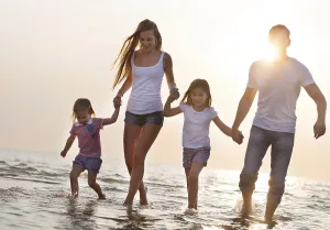 Happy young family having fun running on beach at sunset