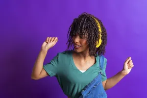 Happy young woman with yellow headphones dancing and enjoying music on a vibrant purple background