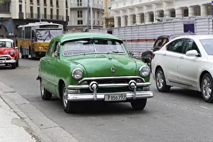 Havana, Cuba, Central America, Green vintage car drives through a city street together with modern cars