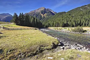 Headwaters Krimml waterfalls. The narrow stream flows between fields and pine forests