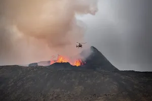 Helicopter flying over smoking active volcanic crater