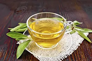 Herbal tea with sage in a glass cup on a burlap napkin on a wooden board background
