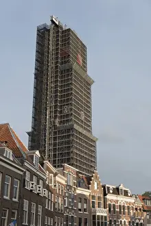 A high-rise building with scaffolding surrounded by traditional brick houses under a blue sky