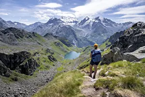 Hiker on hiking trail, mountain lake Lac de Louvie with glaciated summit of the Grand Combin