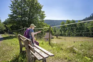 Hiker sitting on bench and pointing to the game reserve on the hiking trail Sprollenhauser Hut