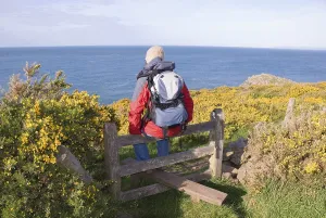 Hiker sitting on a stile, looking out over the sea