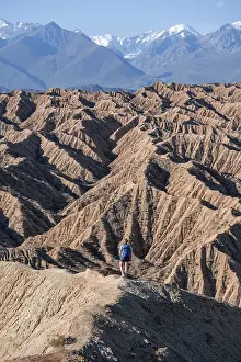 Hiker walking along a canyon, Tian Shan mountains in the background