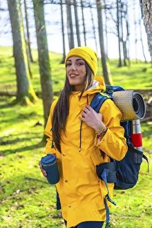 Hiker woman with yellow raincoat and backpack walking in forest