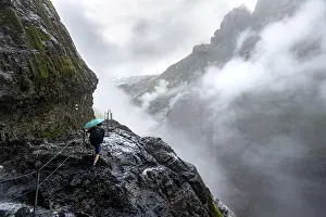 Hikers on a rocky hiking trail Clouds covered in mystical rock gorge with waterfalls