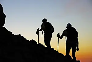 Two hikers in twilight silhouetted as they walk up the active volcano on Stromboli Island