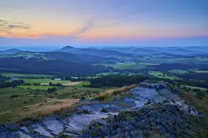 Hilly landscape at dusk with colourful sky and meadows in the foreground