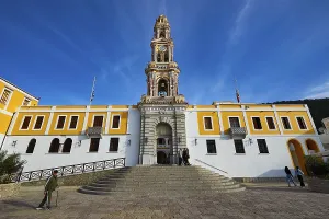 Historic building with baroque church tower and people on a square under blue sky