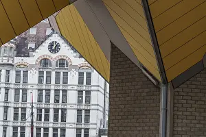 A historic building with a clock is framed by modern architecture with yellow panels