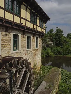 Historic half-timbered house with a large water wheel and river in the background