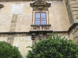 Historical stone building with a small balcony and greenery below the weathered facade