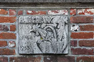 Historical stone relief with a rooster and inscription on a brick wall