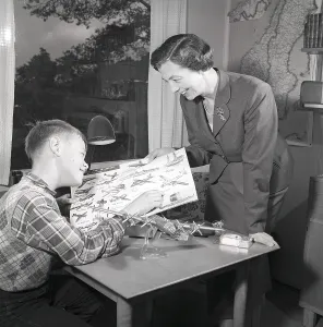 Hobby in the 1950s. A boy is sitting at a table with a plastic model of an American bomb aircraft B29