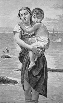 Holiday by the sea, young mother standing with her legs in the water holding her son who is afraid of the sea