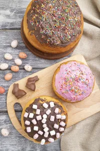 Homemade glazed and decorated easter pies with chocolate eggs and rabbits on a gray wooden background and linen textile