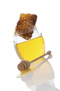 Honey in glass jar with wooden honey spoon and honey comb isolated on white background
