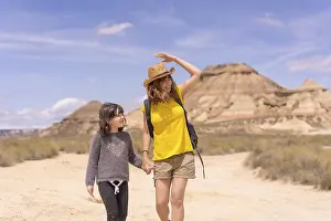 Horizontal frontal view of a mum and girl holding hands strolling for an arid national park