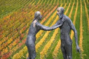 Two human figures as sculptures stand in front of colorful vines in an autumnal atmosphere