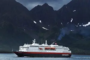 Hurtigruten ship against dramatic mountain backdrop and cloudy sky