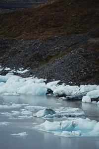 Ice chunks scattered along a rocky shoreline beside still water