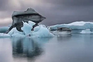 Iceberg formations are reflected in the still water under an overcast sky