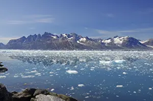 Icebergs floating in crystal clear water with mountains in the background under a blue sky