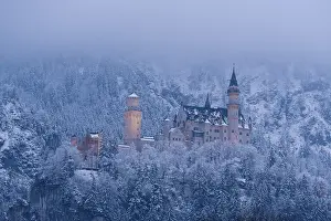 An illuminated castle at dusk, surrounded by snow-covered trees and fog