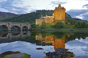 The illuminated Eilean Donan Castle is reflected in the water on a calm evening