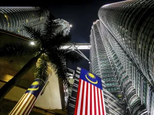 Illuminated skyscraper Petronas Towers at night with the Malaysian flag in the foreground