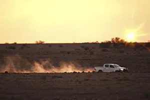 An image of a car on a dusty unsealed road in sunset light mood