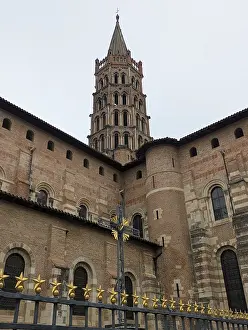 Imposing historic structure with a tall Romanesque tower and brick facade under a cloudy sky