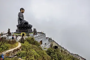 Impressive Buddha statue looks down the steps of a temple complex against a misty mountain backdrop