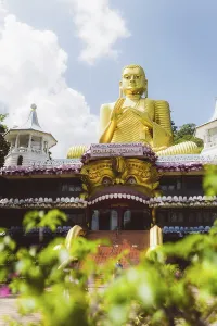 Impressive golden Buddha statue in front of a temple-like background with plants