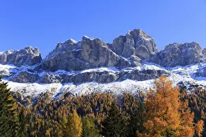 An impressive snow-covered mountain range above autumnal forests and rocks
