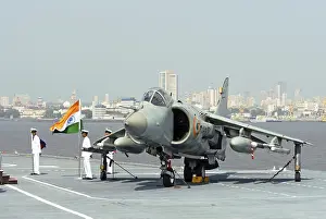 Category Historic EN Prints: Indian navy officer holding national flag next to sea harrier aircraft