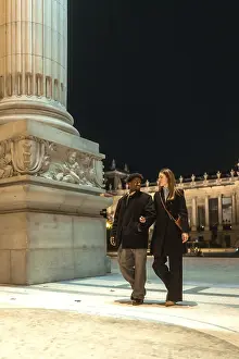 Interracial couple strolling arm in arm past an illuminated historic monument at night